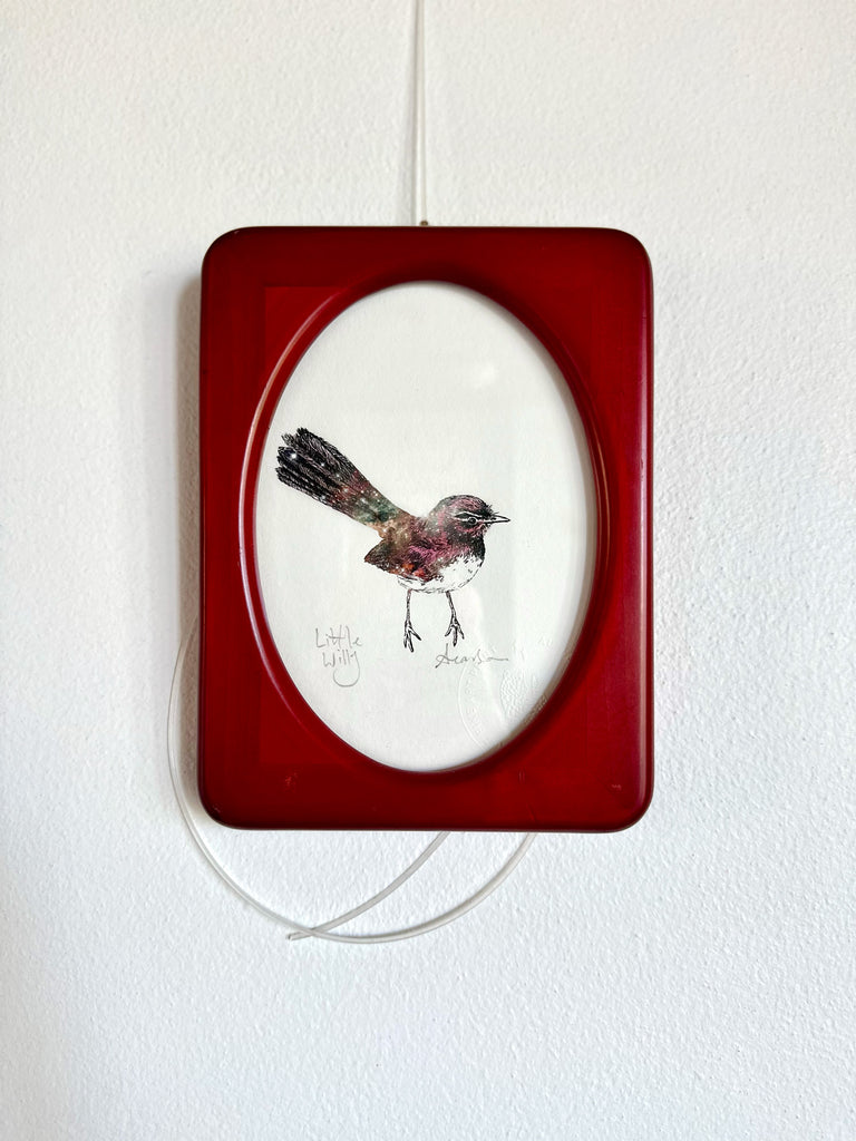 Decorative wall art with a bird illustration in a red frame on a white wall.