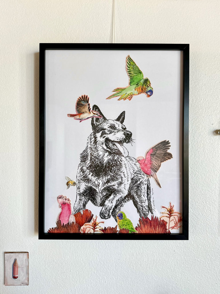 Framed artwork of a dog with birds and flowers on a white wall.